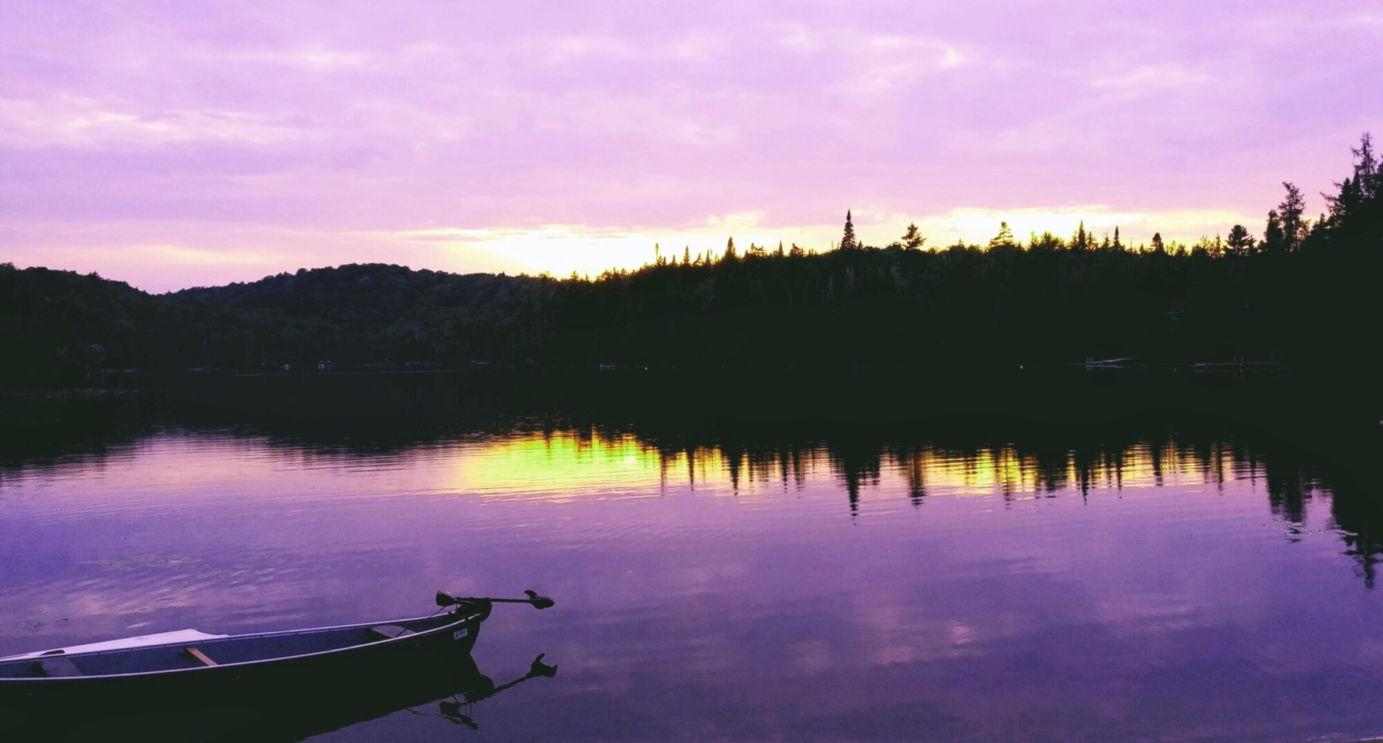 Image of a canoe on a lake with a purple hue in the sky reflected in the water